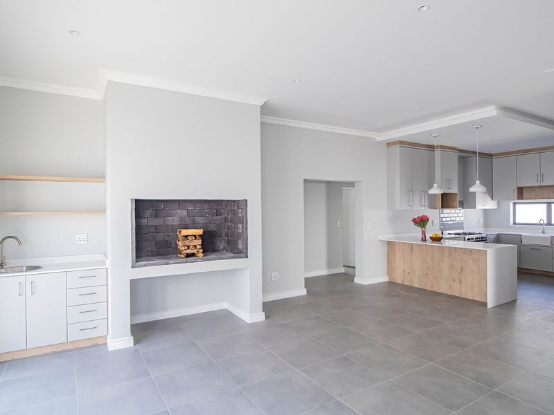 Spacious open-plan living area featuring a modern kitchen with island, stone countertops, and a built-in fireplace, finished with neutral tones and tiled flooring.