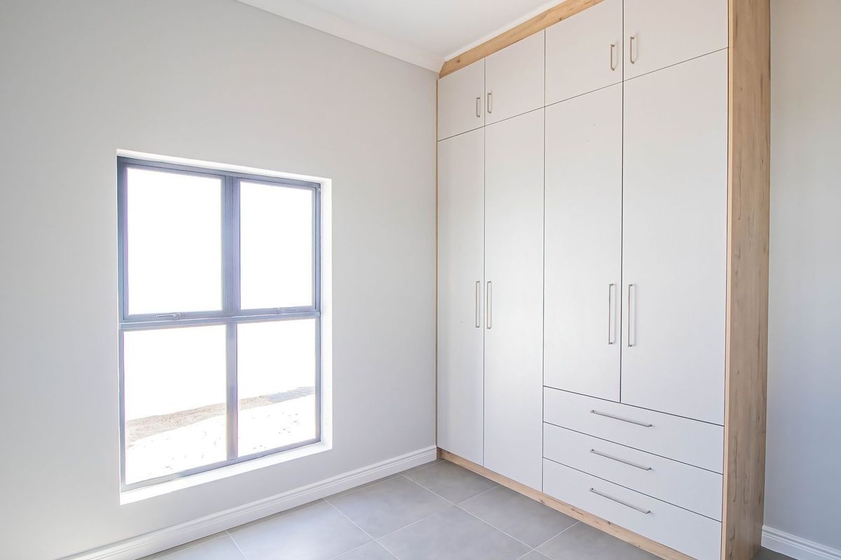 A bright, modern bedroom featuring neutral walls, tiled flooring, and extensive built-in cabinetry with integrated storage.
