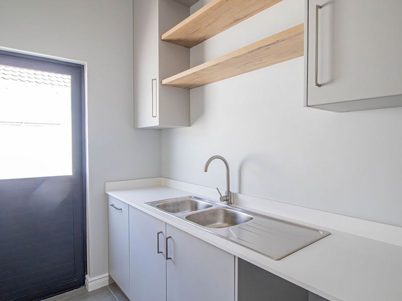 A clean, modern scullery featuring built-in cabinetry, a stainless steel double sink with a gooseneck mixer, and open wooden shelving.