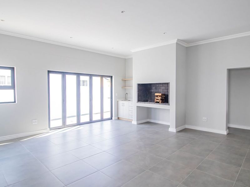 Spacious open-plan living area featuring large bi-fold doors, tiled flooring, recessed lighting, and a built-in fireplace with adjacent cabinetry and sink.
