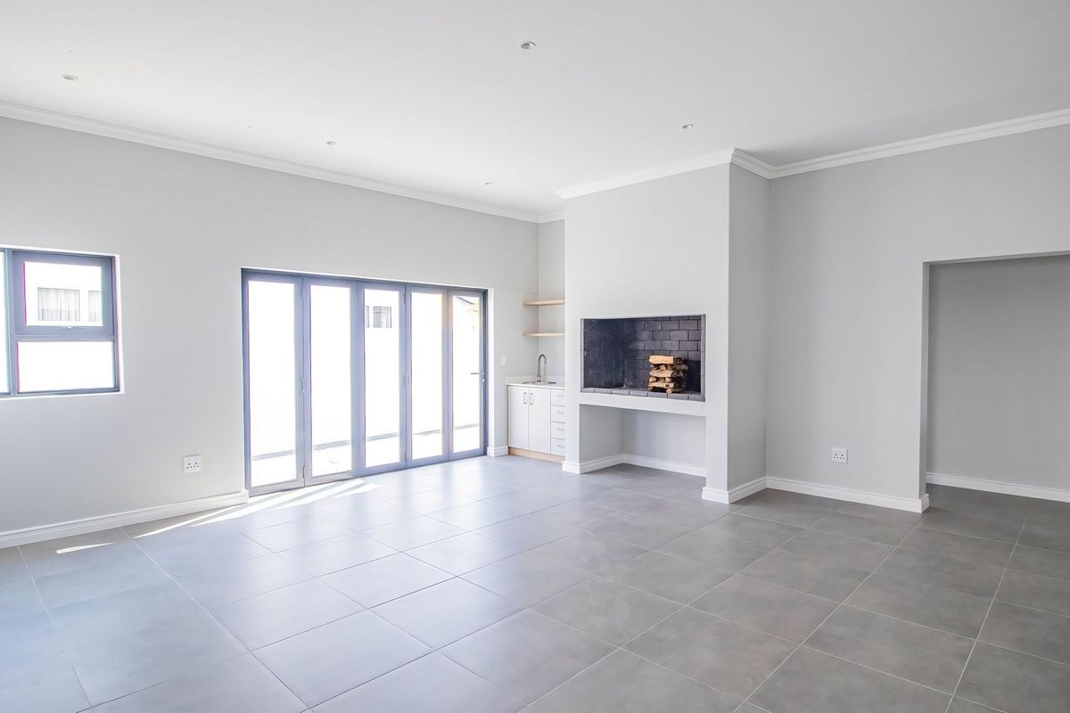 Spacious open-plan living area featuring large bi-fold doors, tiled flooring, recessed lighting, and a built-in fireplace with adjacent cabinetry and sink.