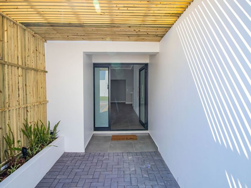 A modern, covered entrance featuring a timber slat pergola, privacy screen, built-in planter box, and a contemporary glass panel front door.