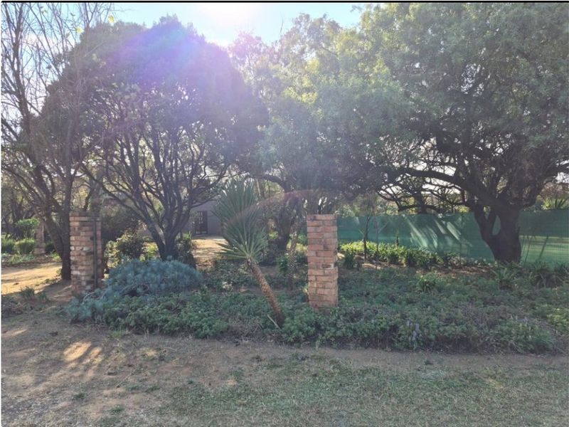 A mature garden area featuring established trees, landscaped ground cover, and decorative brick pillars.