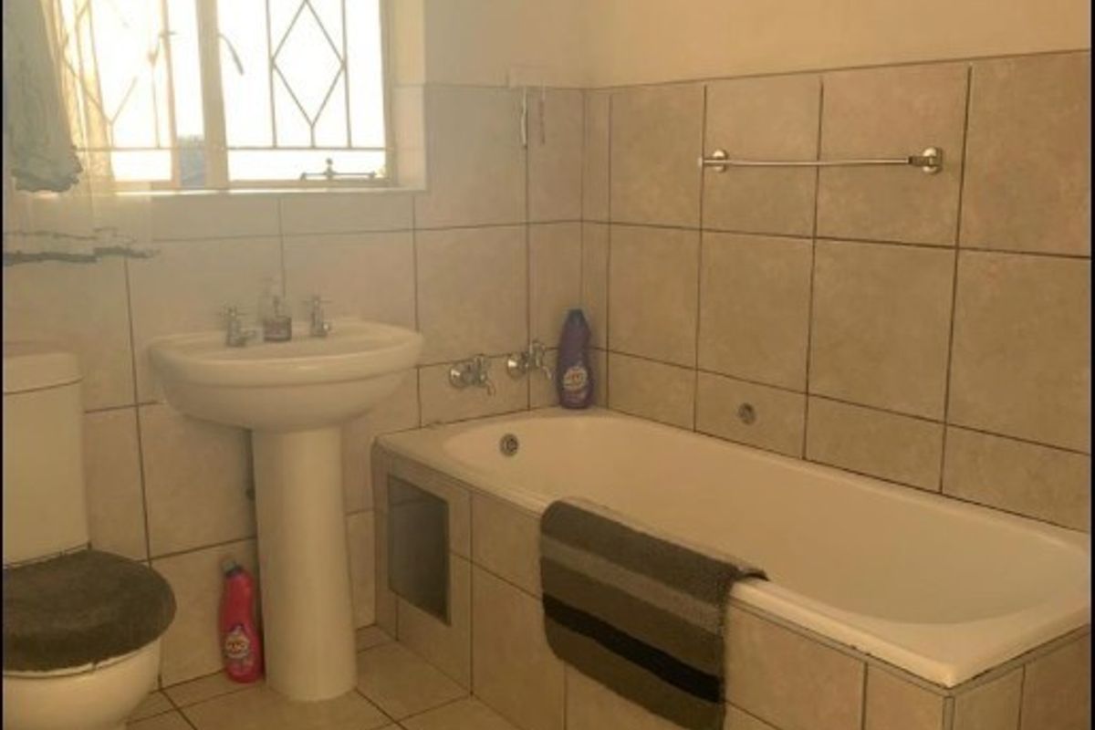 A functional bathroom featuring a pedestal washbasin, a built-in bathtub with tiled surround, and neutral ceramic wall and floor tiling.