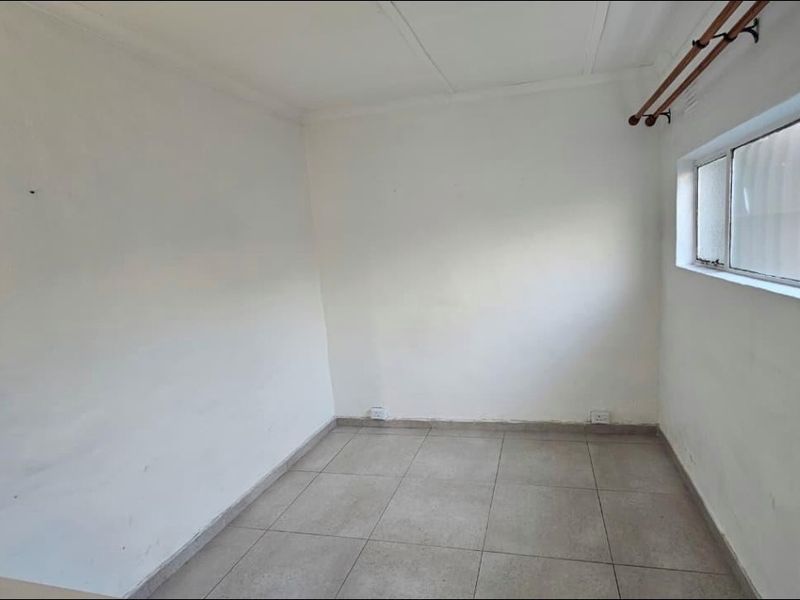 An empty bedroom featuring neutral tiled flooring and a curtain rod, providing a blank canvas for potential interior design and furnishing.