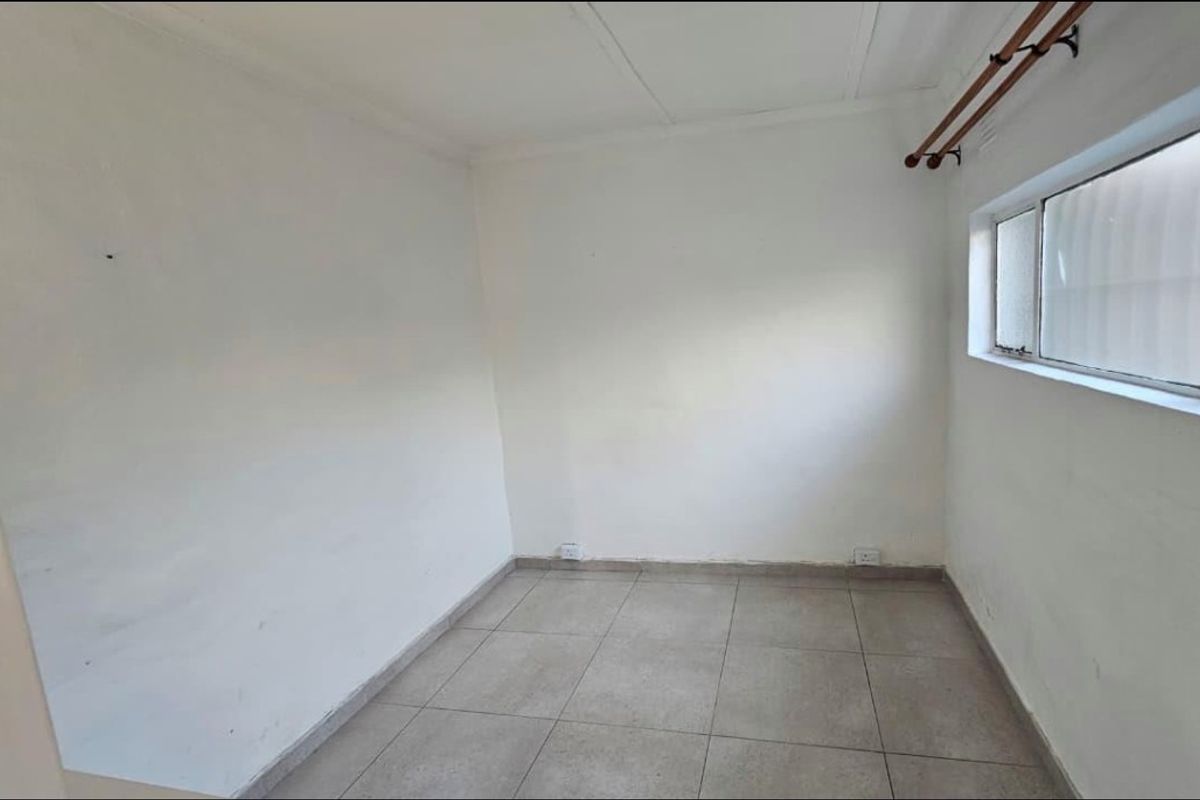 An empty bedroom featuring neutral tiled flooring and a curtain rod, providing a blank canvas for potential interior design and furnishing.