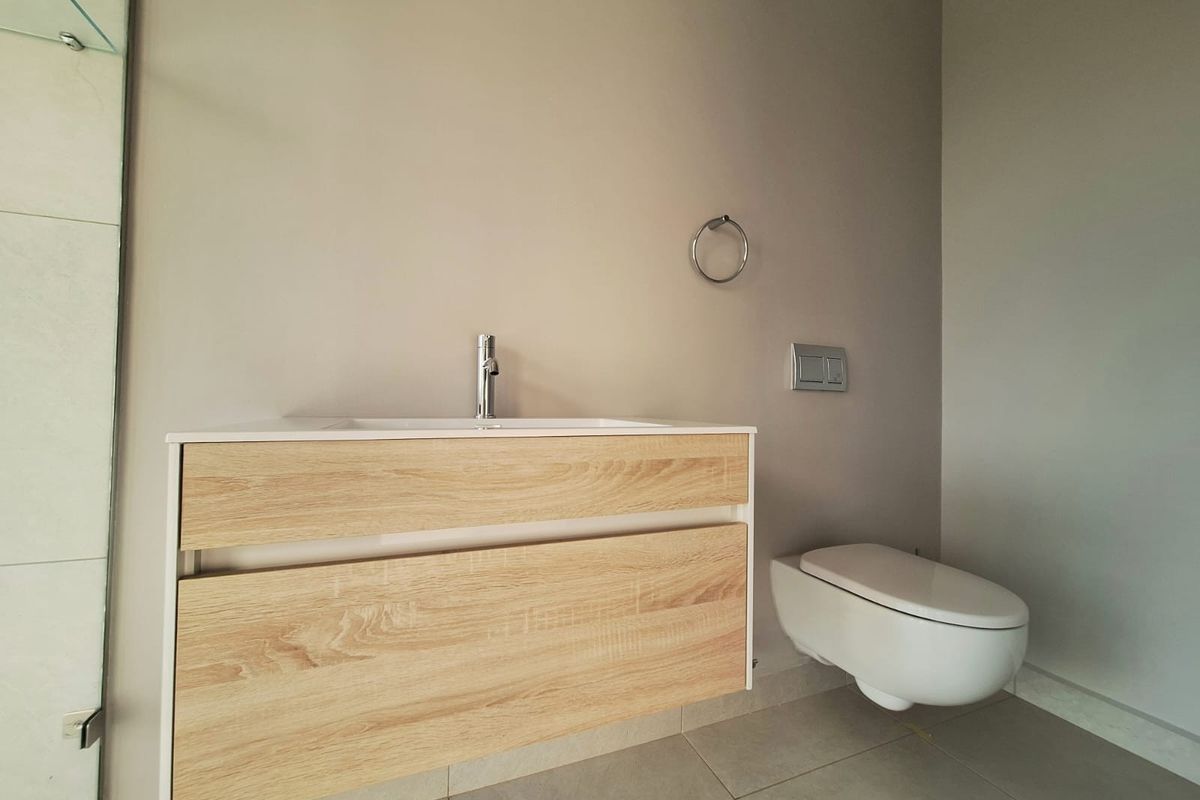 Modern bathroom featuring a wall-mounted wood-finish vanity with basin and a sleek wall-hung toilet with concealed cistern.