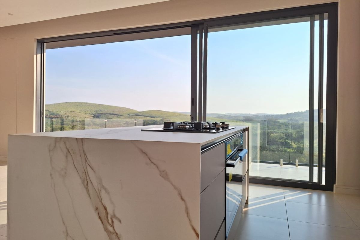 Modern kitchen island featuring a stone countertop, built-in oven, and gas hob, set against large sliding glass doors with scenic landscape views.