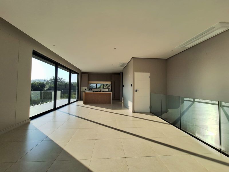 Spacious open-plan living area featuring large sliding glass doors, modern tiled flooring, a glass balustrade, and a sleek kitchen island with built-in cabinetry.