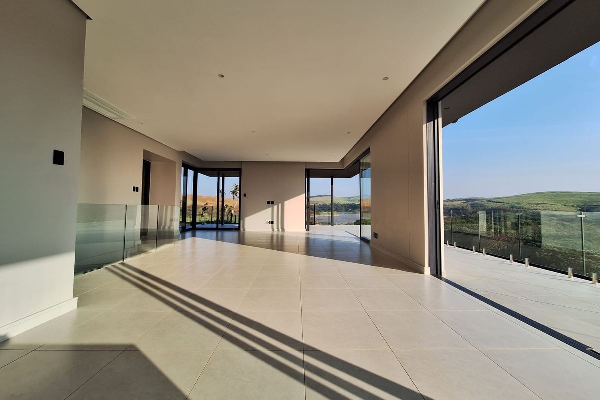 Spacious, modern open-plan living area featuring large format floor tiles, recessed lighting, and expansive sliding glass doors opening to a scenic balcony.