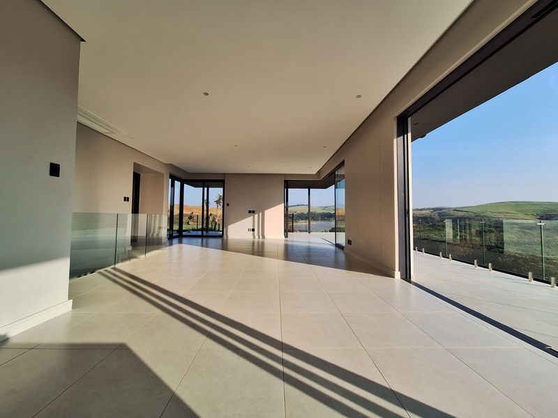 Spacious, modern open-plan living area featuring large format floor tiles, recessed lighting, and expansive sliding glass doors opening to a scenic balcony.