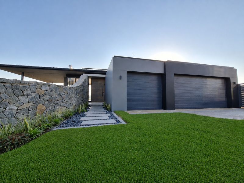 Modern front facade featuring a double garage, striking stone feature wall, and a clean, landscaped entrance walkway.