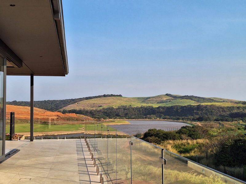 Spacious covered patio featuring modern tiled flooring and a frameless glass balustrade, offering expansive views of the surrounding landscape and water.