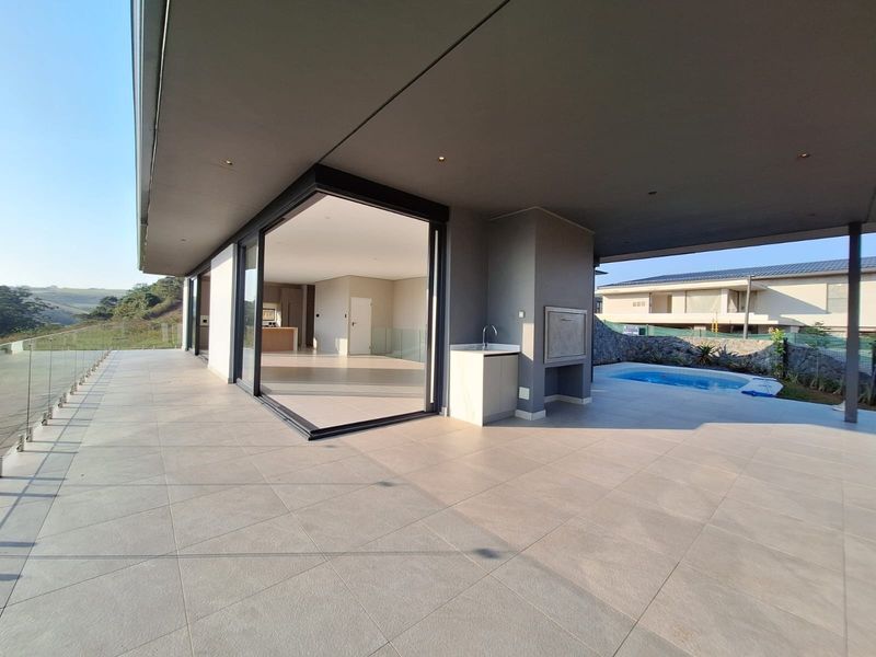 Spacious covered patio featuring a built-in braai, outdoor sink, and glass balustrades, offering seamless indoor-outdoor flow through large sliding doors.