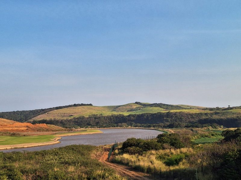 A scenic view of a natural landscape featuring a water body, rolling hills, and surrounding vegetation.