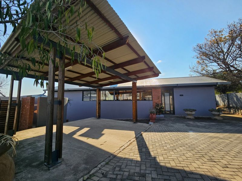 Front exterior view featuring a covered carport with timber supports, paved driveway, and brick accents against the main building facade.