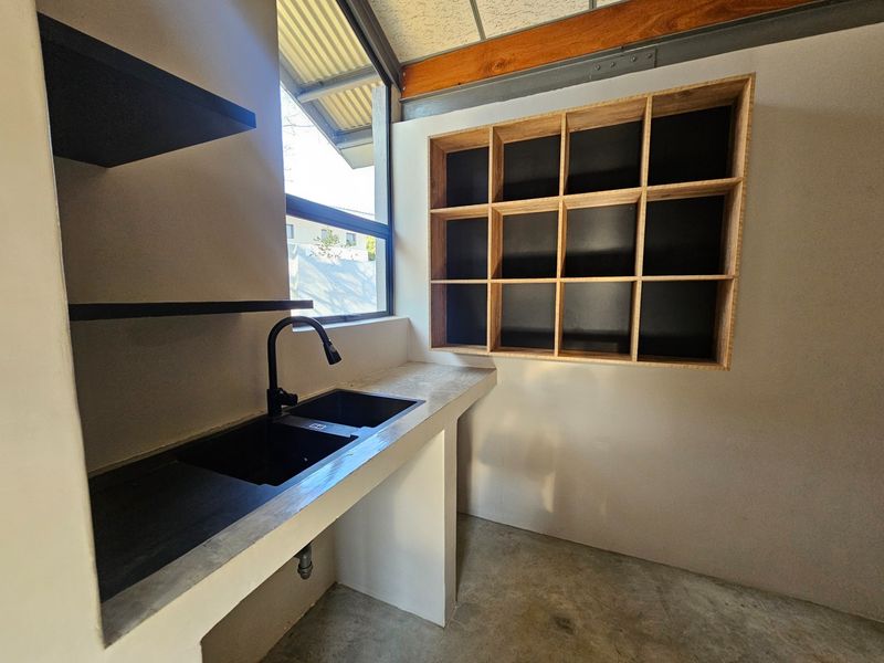 A modern scullery featuring a concrete countertop, black sink, and custom built-in wooden shelving, offering a clean and functional prep or wash-up area.