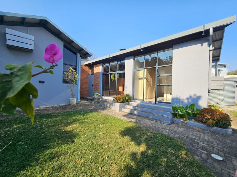 Rear view of the property featuring a paved patio area, large glass sliding doors, and modern plastered exterior walls.