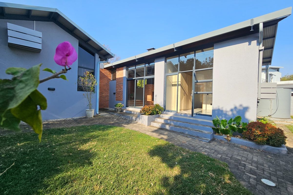 Rear view of the property featuring a paved patio area, large glass sliding doors, and modern plastered exterior walls.