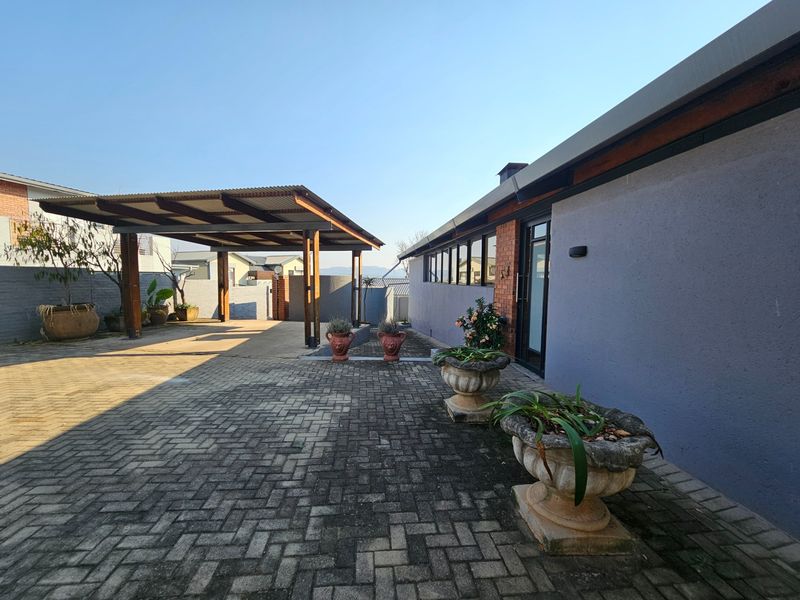 Rear exterior view featuring a paved driveway, a covered carport structure, and brick and rendered wall finishes.