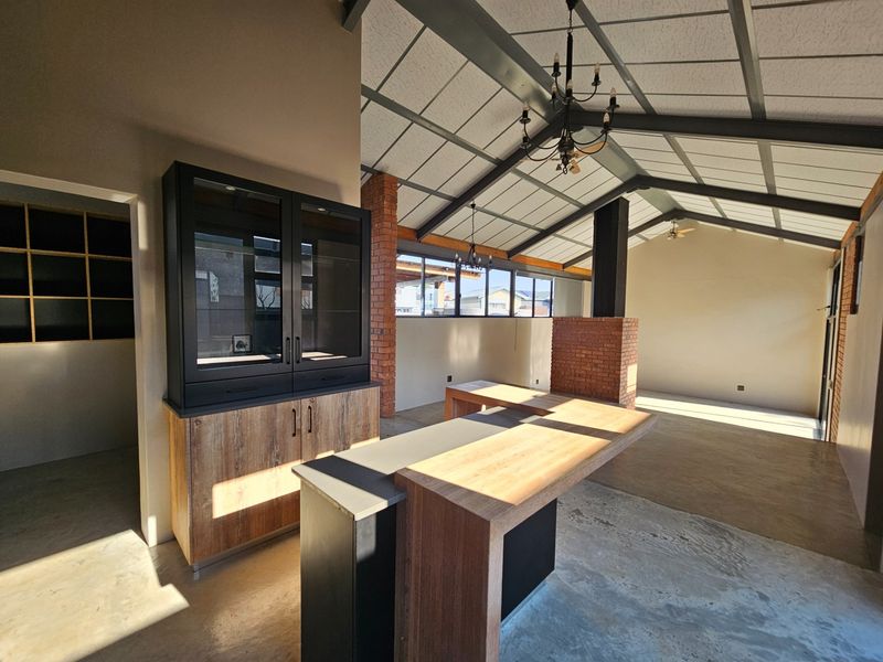 Spacious open-plan living area featuring vaulted ceilings with exposed trusses, a brick fireplace, concrete floors, and a modern kitchen island with built-in cabinetry.
