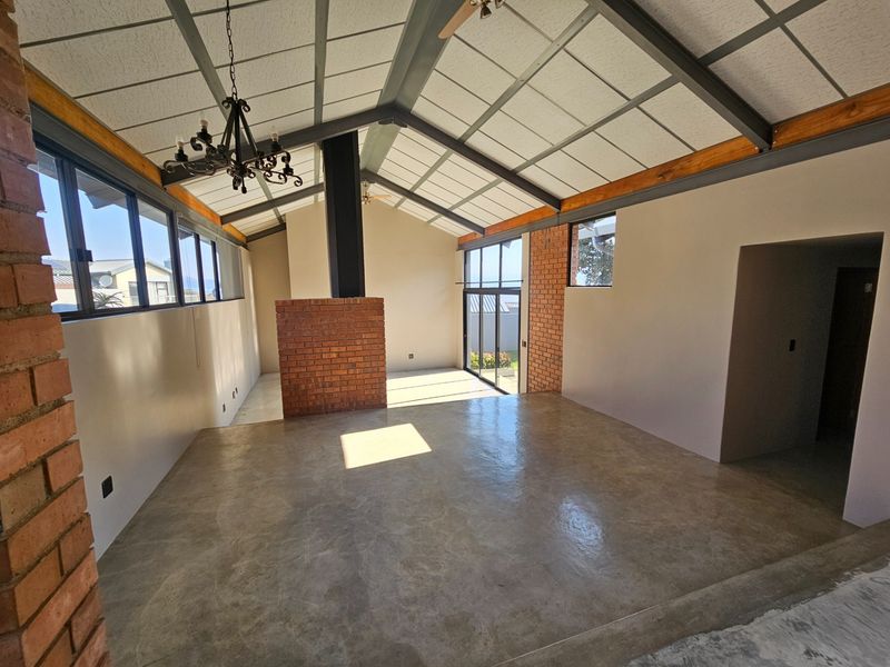 Spacious open-plan living area featuring vaulted ceilings with exposed steel beams, a central brick fireplace, and polished concrete floors with large glass sliding doors.