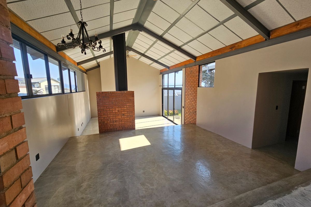 Spacious open-plan living area featuring vaulted ceilings with exposed steel beams, a central brick fireplace, and polished concrete floors with large glass sliding doors.