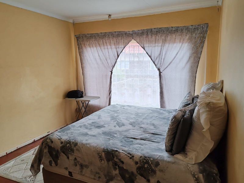 A bedroom featuring a window with security bars and yellow painted walls, requiring cosmetic updates to improve the overall aesthetic.