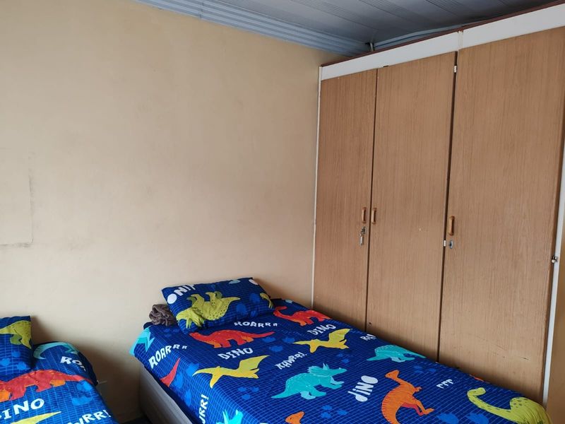 A bedroom featuring a built-in wooden wardrobe and plain wall finishes, providing functional storage space.
