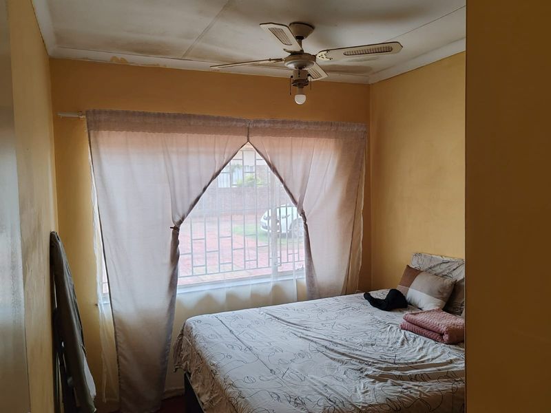 A bedroom featuring a ceiling fan and security bars on the window, showing signs of ceiling wear and peeling paint.