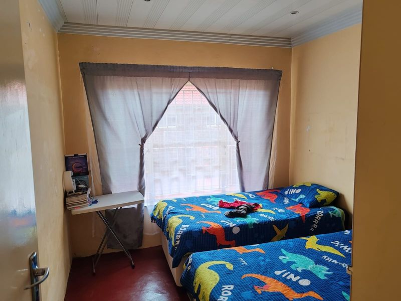 A bedroom featuring a panelled ceiling, recessed lighting, and security bars on the window. The room requires cosmetic updates to the wall finishes.