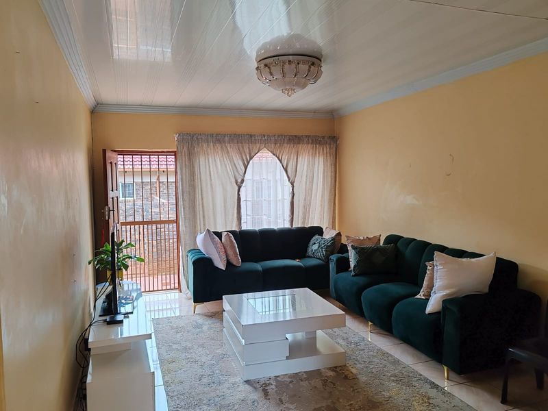 A living room featuring tiled flooring, a glossy PVC ceiling with a decorative light fixture, and access to an exterior security gate.