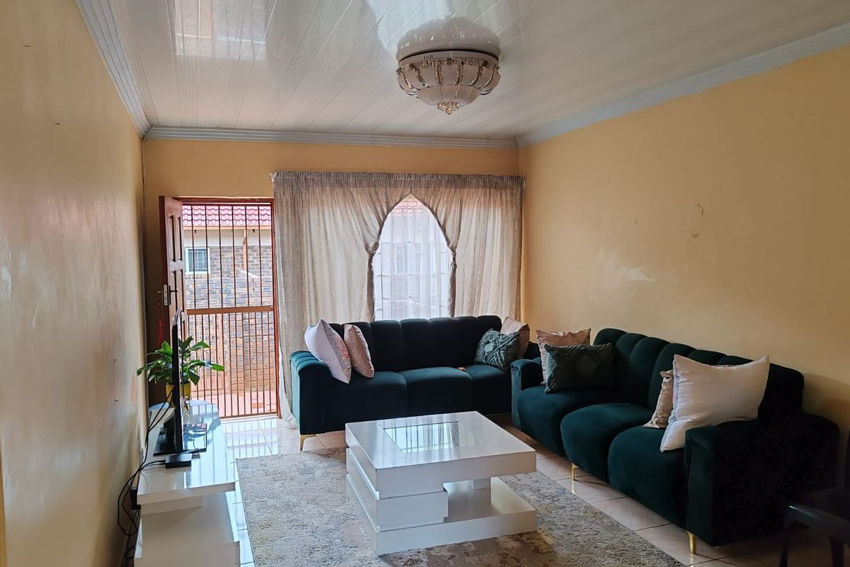 A living room featuring tiled flooring, a glossy PVC ceiling with a decorative light fixture, and access to an exterior security gate.