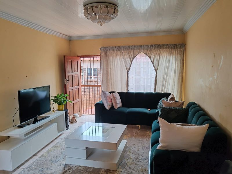 A living room featuring tiled flooring, a central ceiling light fixture, and a security gate leading to the exterior.