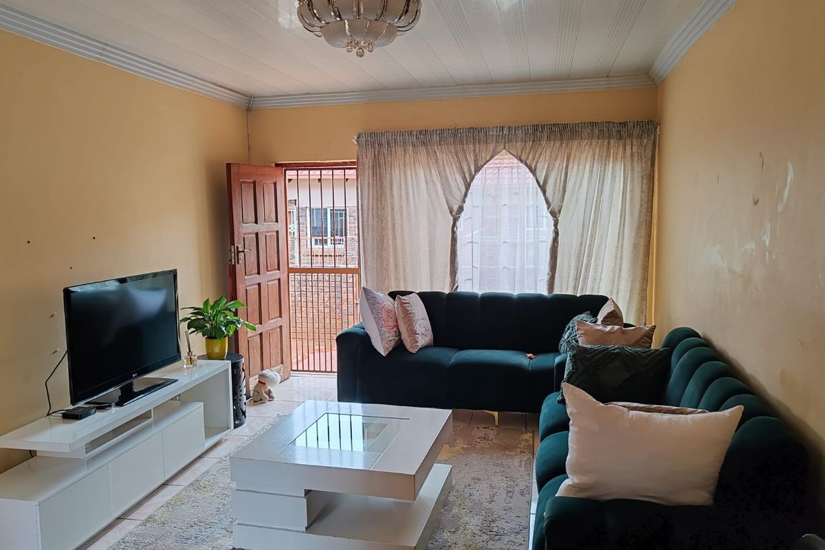 A living room featuring tiled flooring, a central ceiling light fixture, and a security gate leading to the exterior.