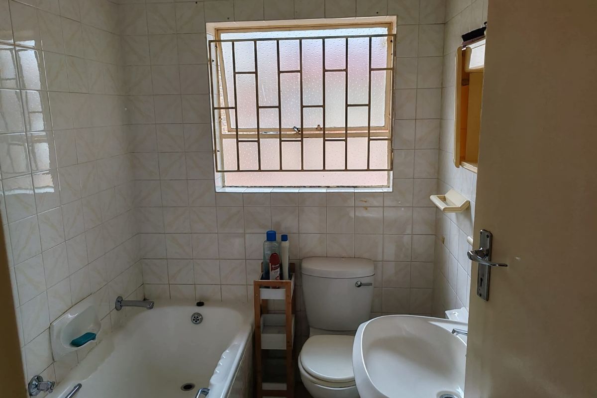 A compact bathroom featuring a bathtub, pedestal basin, and toilet, finished with dated wall tiles and fitted with security bars on the window.