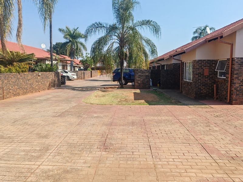 Exterior view of a townhouse complex featuring facebrick facades, tiled roofs, and paved driveway access.