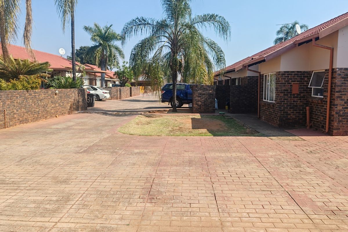 Exterior view of a townhouse complex featuring facebrick facades, tiled roofs, and paved driveway access.