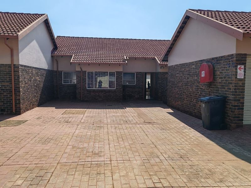 A paved front courtyard area of a townhouse featuring facebrick walls, tiled roofing, and secure access points.