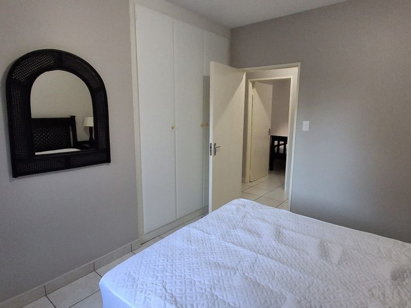 A bedroom featuring neutral wall tones, tiled flooring, and built-in cupboards, offering a clean and functional living space.