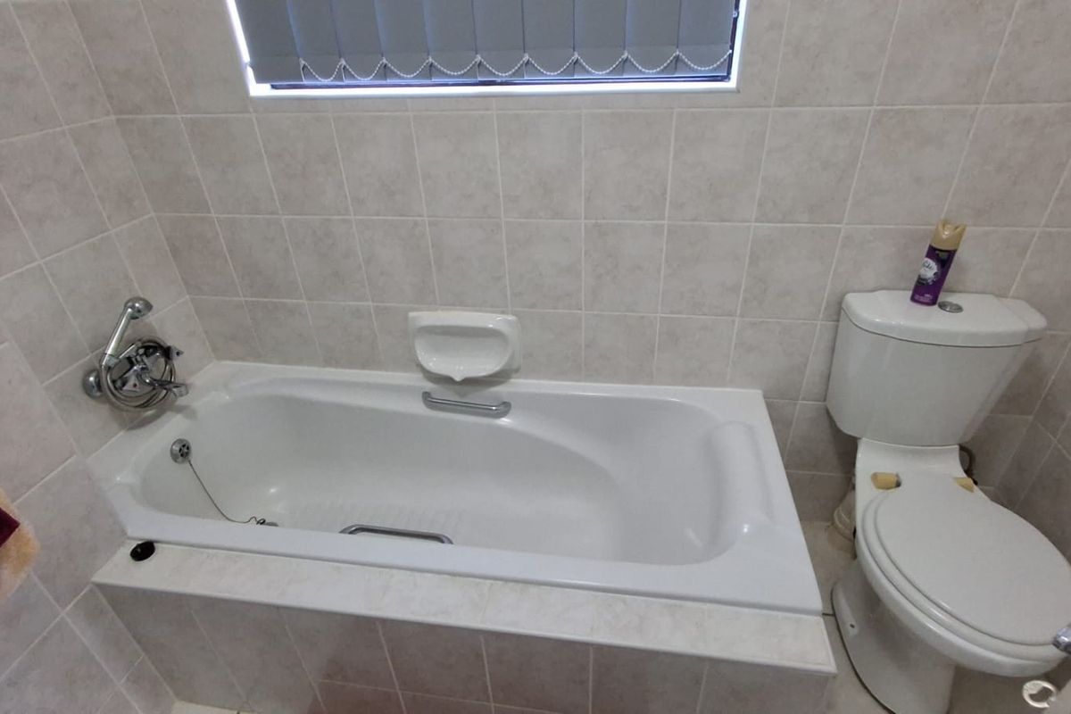 A functional bathroom featuring a built-in bathtub with shower attachment, tiled walls, and a standard toilet.