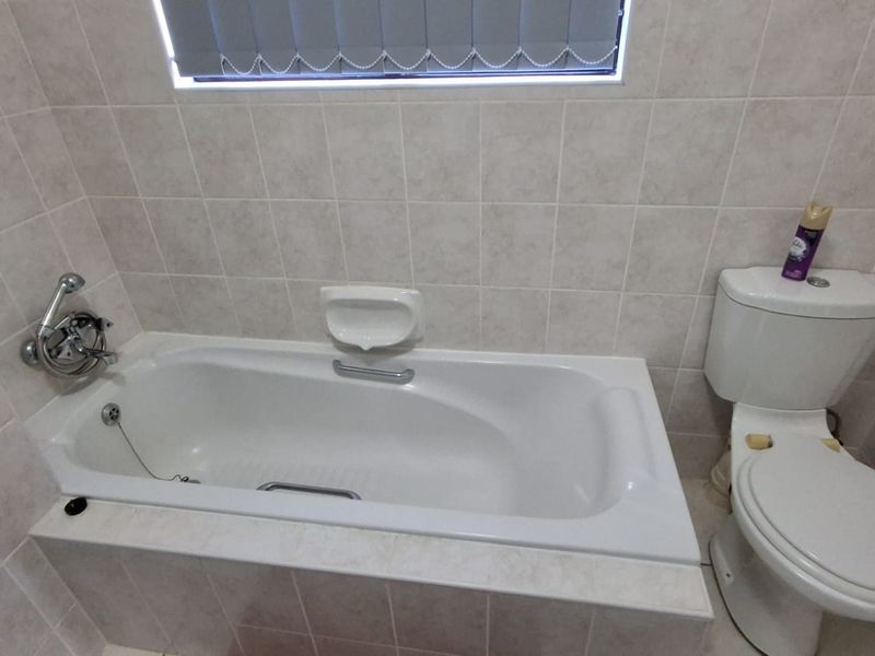 A functional bathroom featuring a built-in bathtub with shower attachment, tiled walls, and a standard toilet.