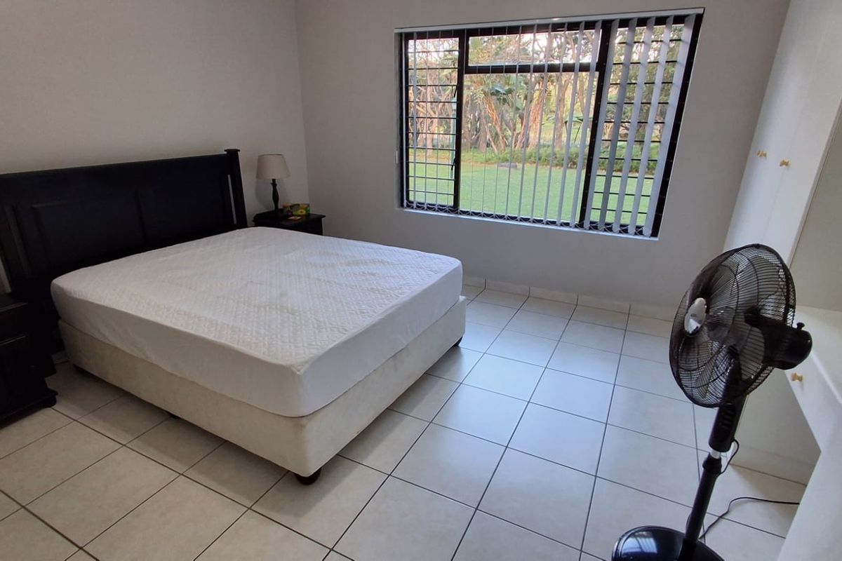 A functional bedroom featuring tiled flooring, built-in cupboards, and a large window with security bars overlooking the garden.