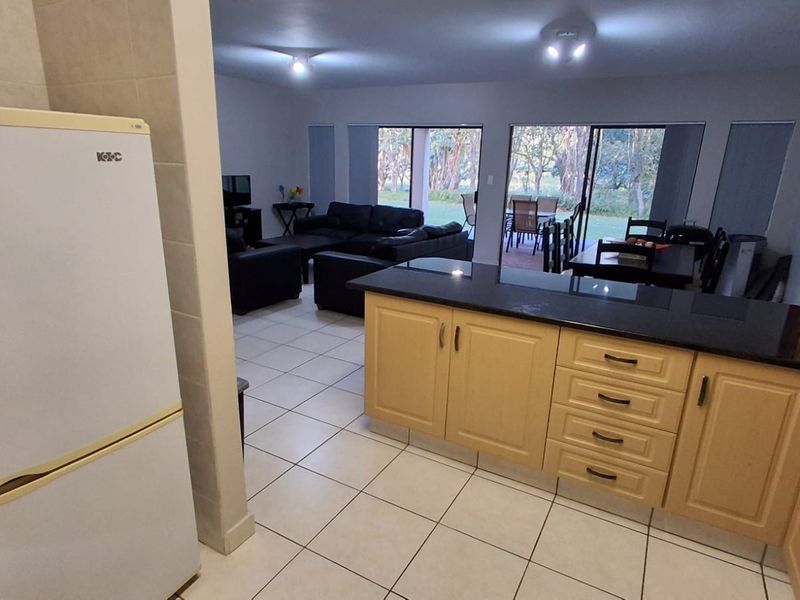 Open-plan living area featuring a kitchen with granite countertops and wooden cabinetry, flowing into a lounge space with direct access to the patio.