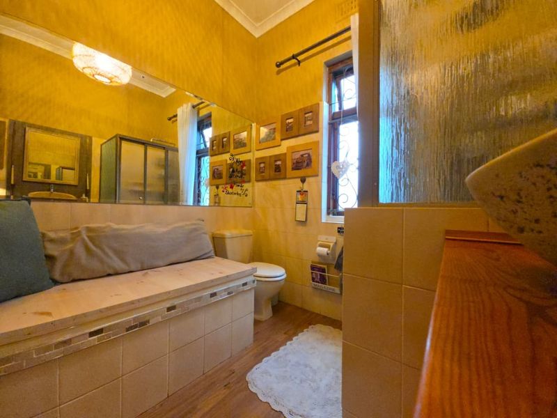 A functional bathroom featuring tiled walls, a built-in tiled bench, a large wall mirror, and a shower enclosure with a timber-framed window.