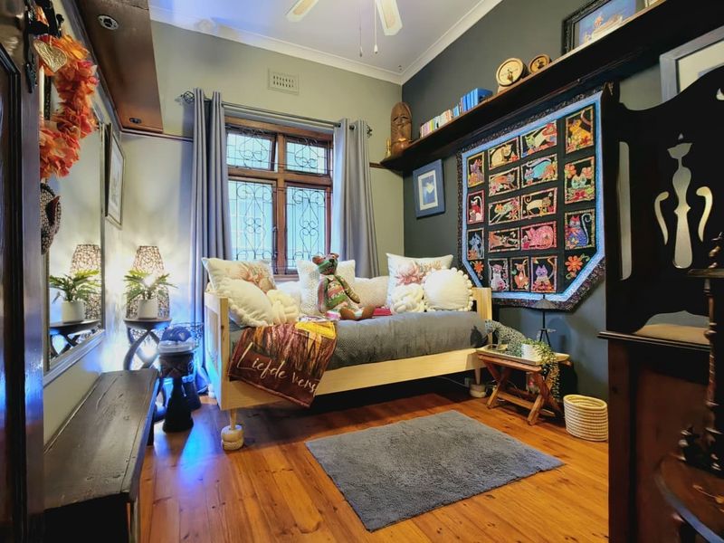 A cozy bedroom featuring polished timber flooring, a classic leaded glass window, and a built-in wall shelf, finished with a ceiling fan.