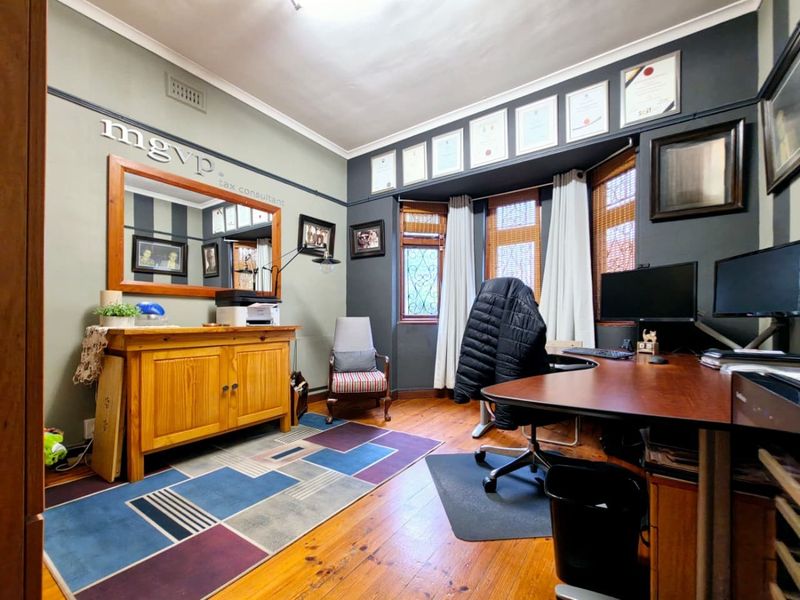 A home office featuring polished timber flooring, a bay window with natural light, and classic picture rail detailing.