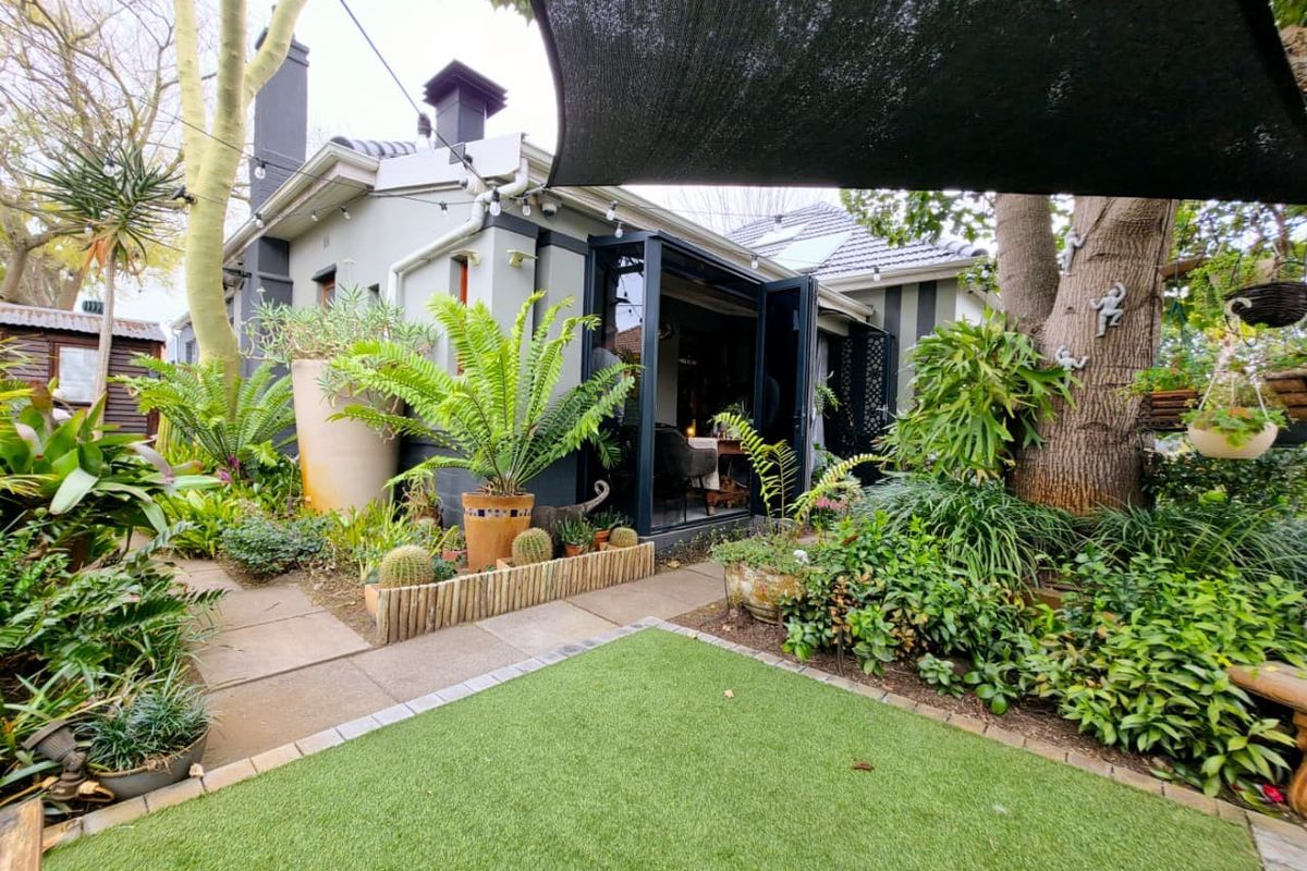 A well-maintained rear garden featuring artificial lawn, paved pathways, and bi-fold doors leading into the home, shaded by a large overhead sail.