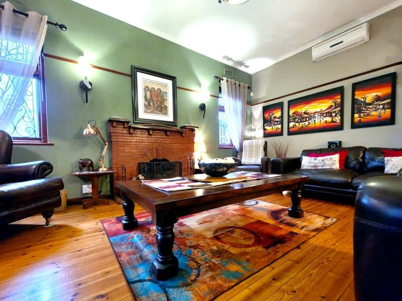 A cozy living room featuring a classic brick fireplace, polished hardwood flooring, and a wall-mounted air conditioning unit for climate control.