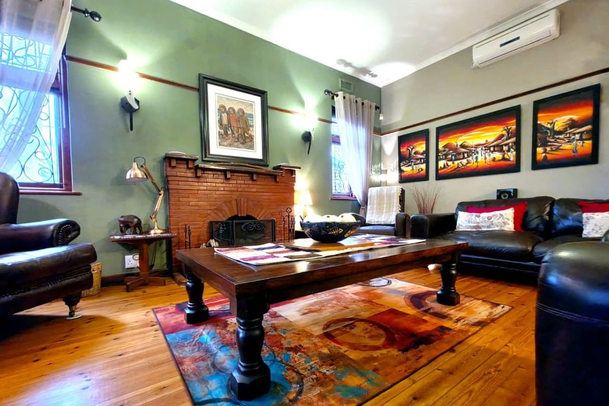A cozy living room featuring a classic brick fireplace, polished hardwood flooring, and a wall-mounted air conditioning unit for climate control.